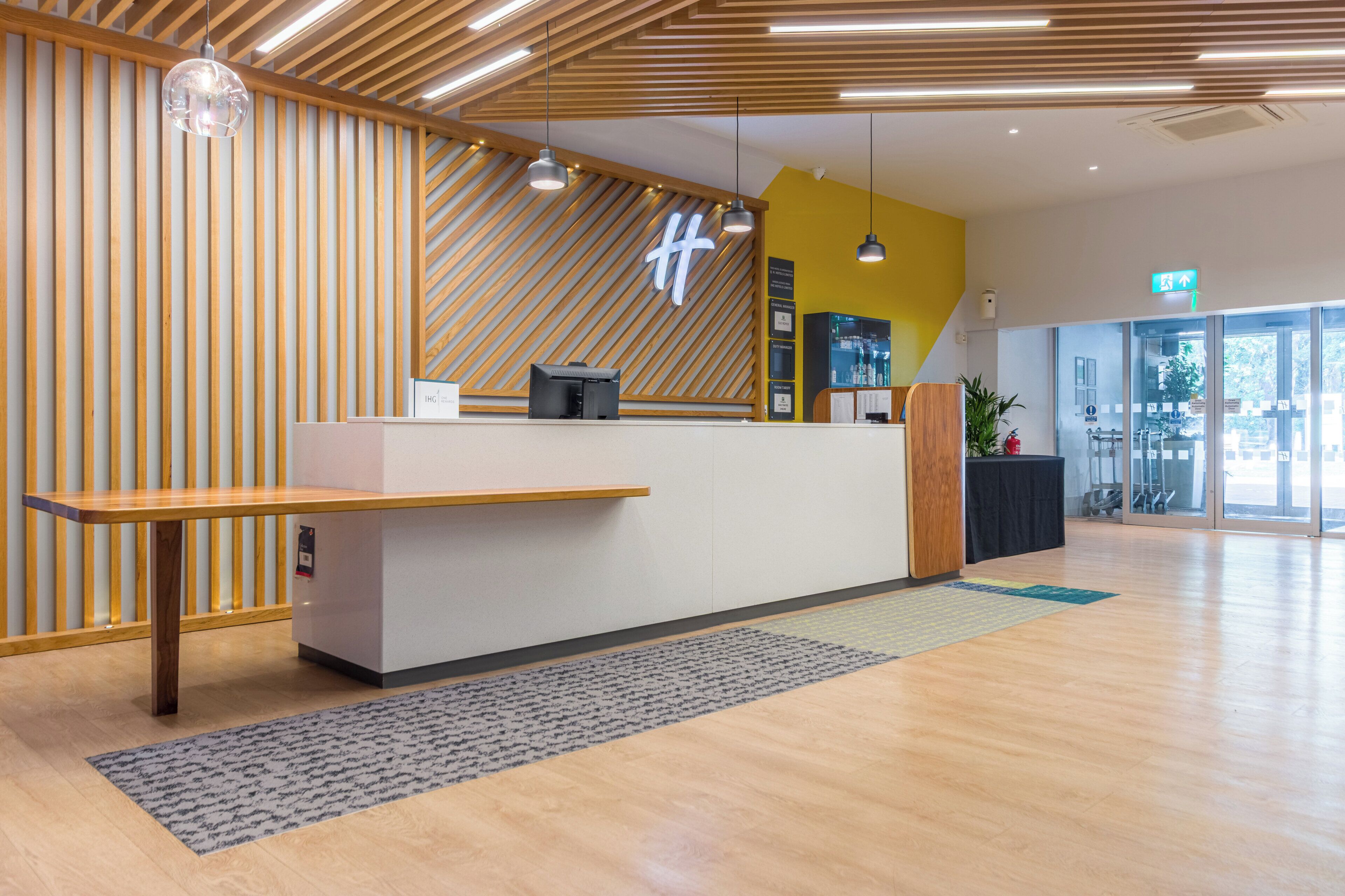 A reception desk with a modern design, a wooden slat wall, and a glass door leading outside.
