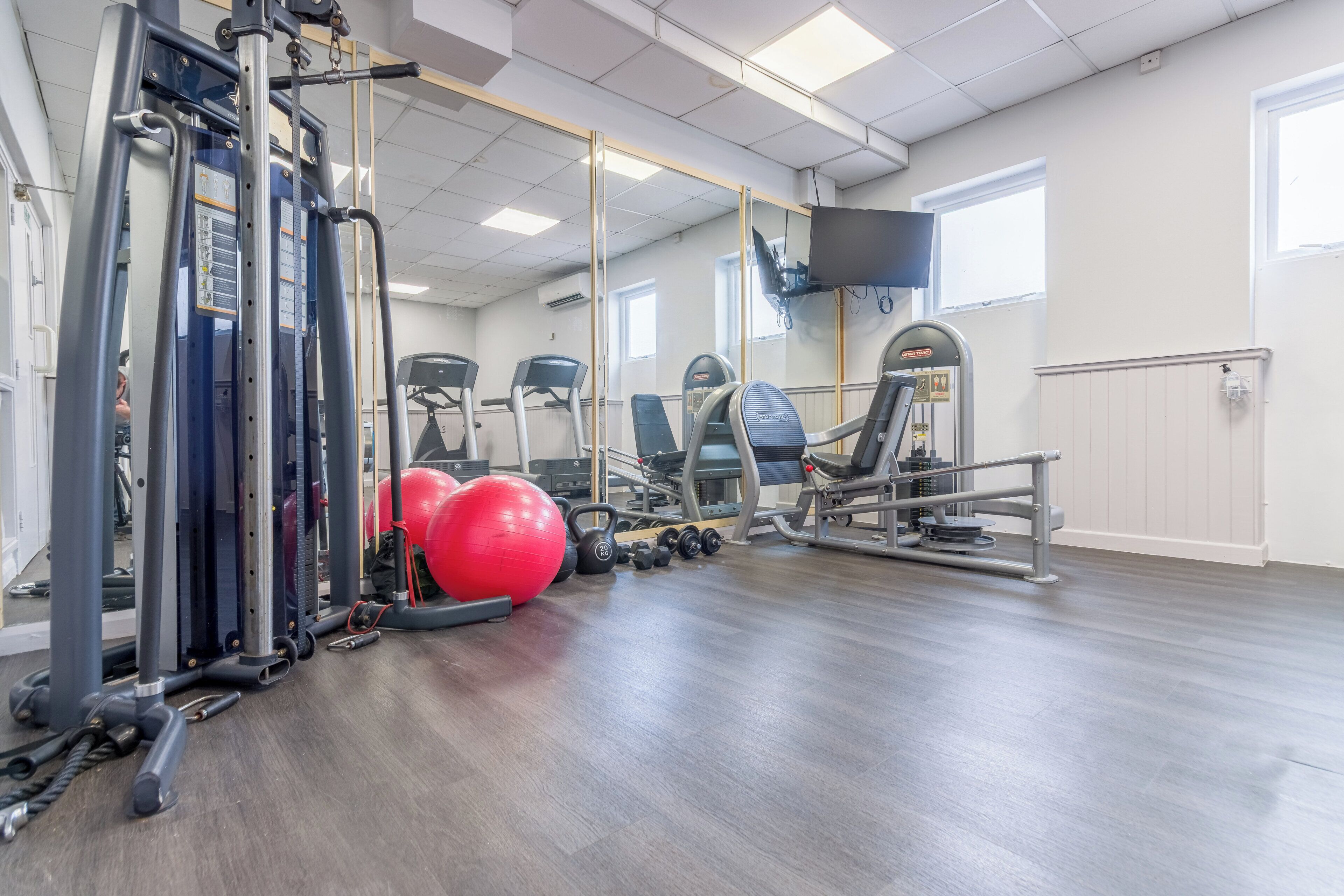 A gym with exercise equipment, a mirror, and a red exercise ball.
