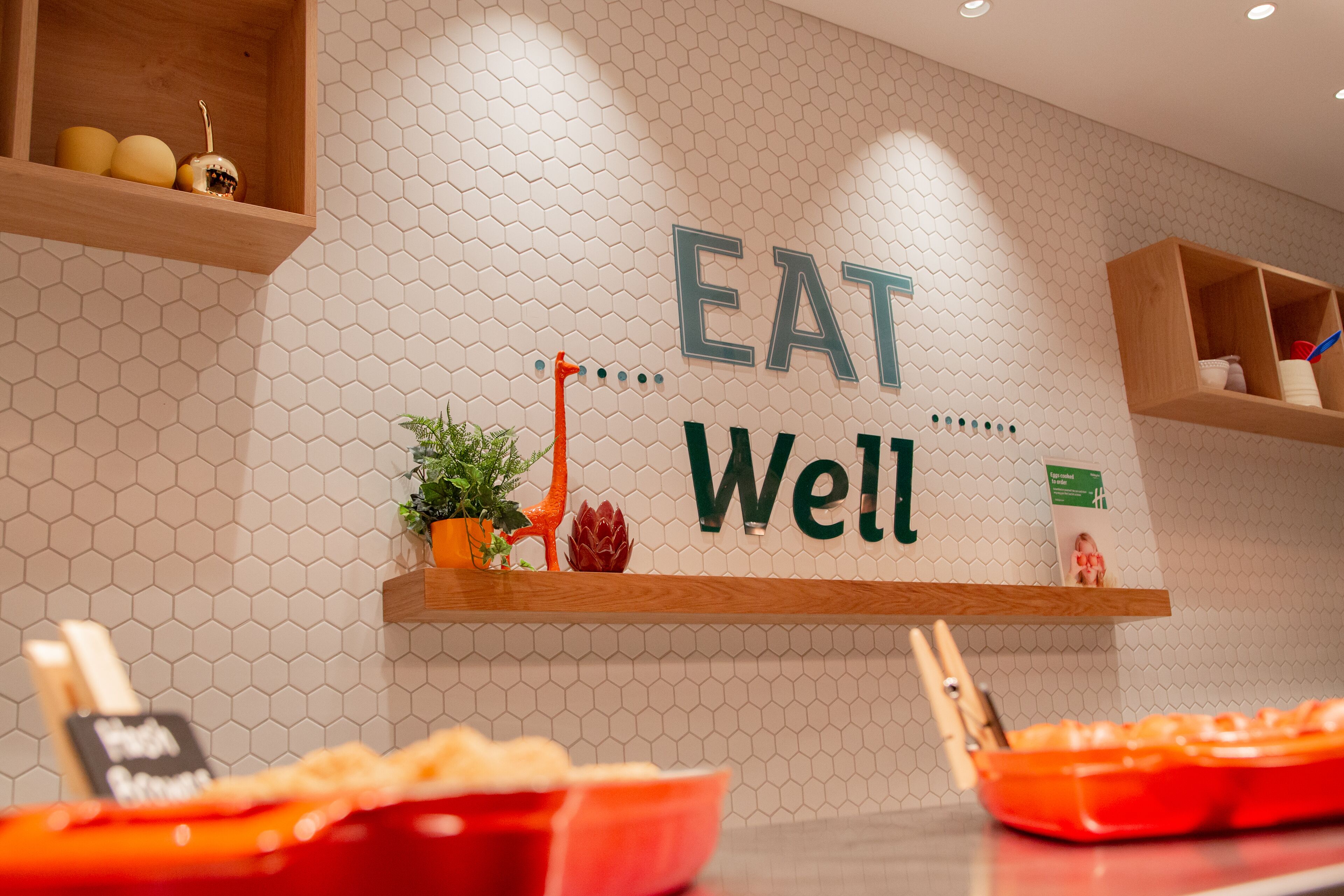 A kitchen with a hexagonal tile backsplash, wooden shelves, and a sign that reads "EAT Well".