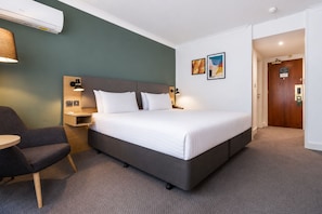 Una habitación de hotel con una cama, mesitas de noche, una silla y obras de arte en la pared.