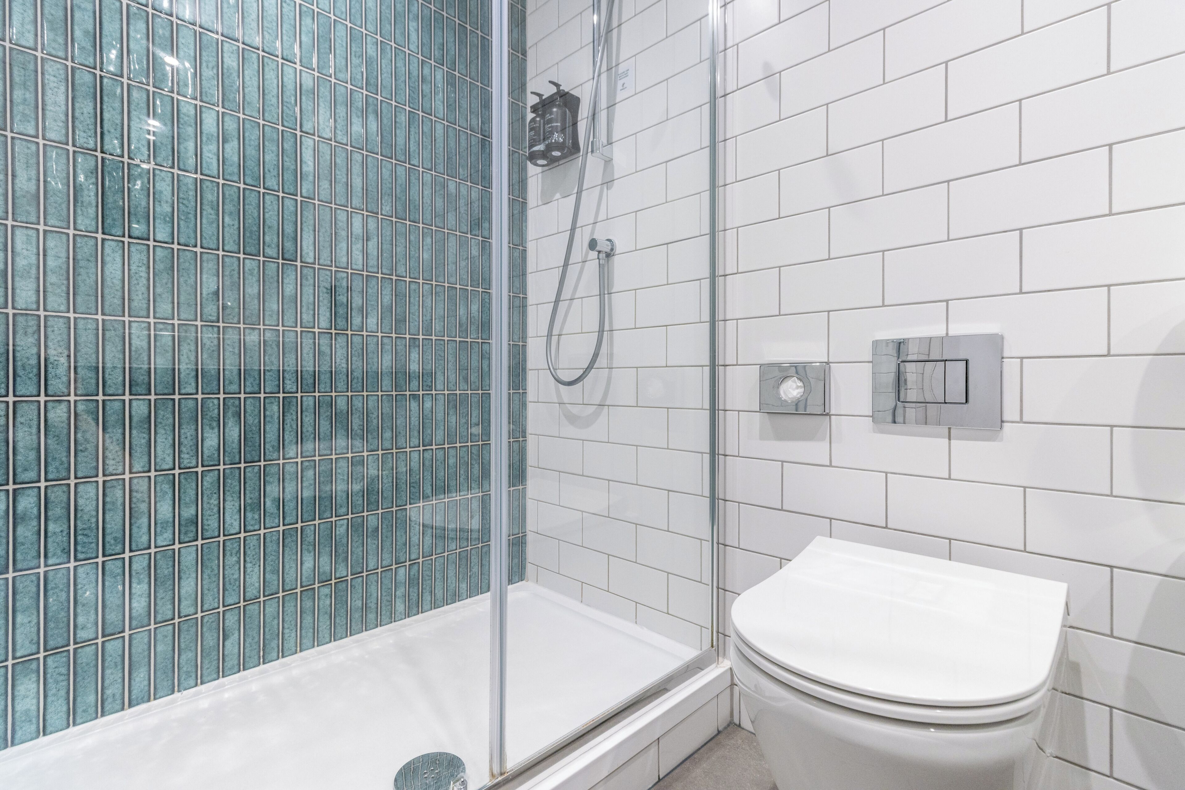 Ein Badezimmer mit Duschkabine aus Glas, einer weißen Toilette und einer am Wand befestigten Duschbrause.