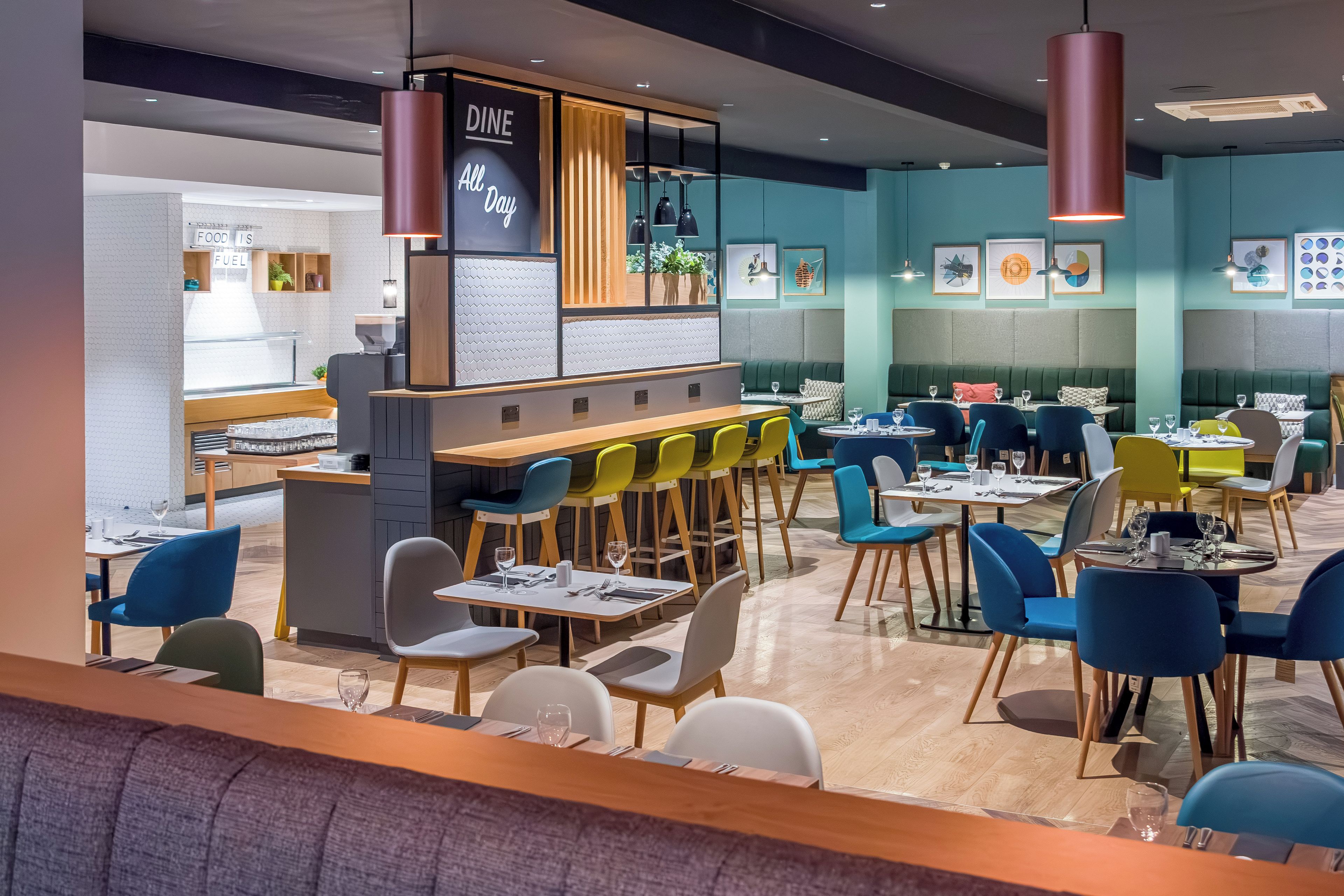 Interior moderno de restaurante con barra, diferentes disposiciones de asientos y un letrero que dice 'Dine All Day'.