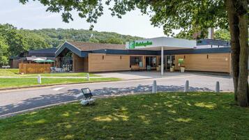 Ein Hotel Holiday Inn mit modernem Design, mit einer überdachten Außenbereich-Sitzgelegenheit und einem gepflegten Rasen.