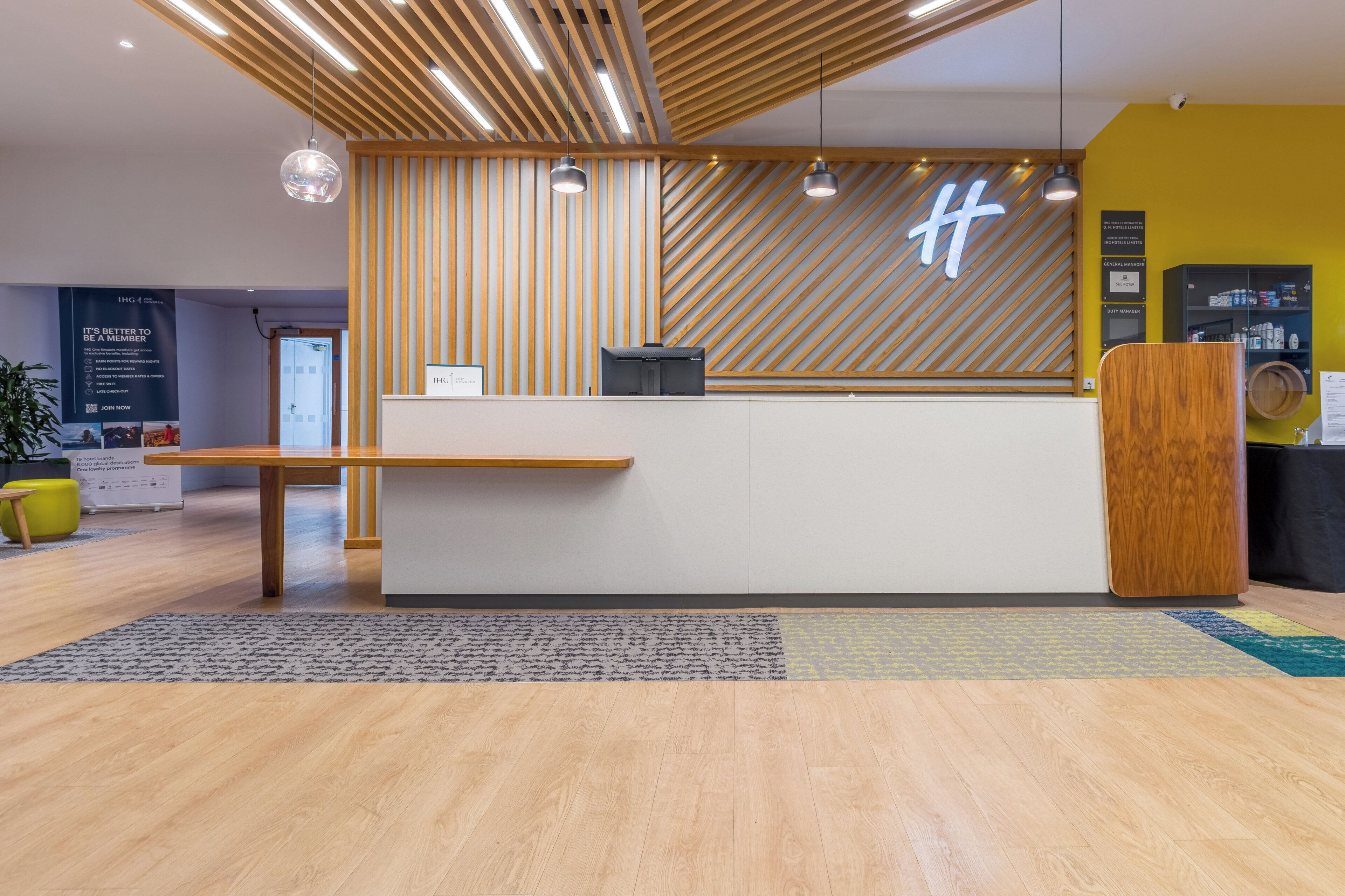 A hotel reception desk with a modern design, featuring a wooden slat wall and a digital display.