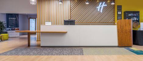 A hotel reception desk with a modern design, featuring a wooden slat wall and a digital display.