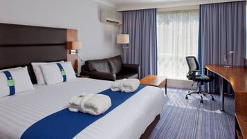 A hotel room with a large bed, a desk, a chair, a lamp, and a window with curtains.