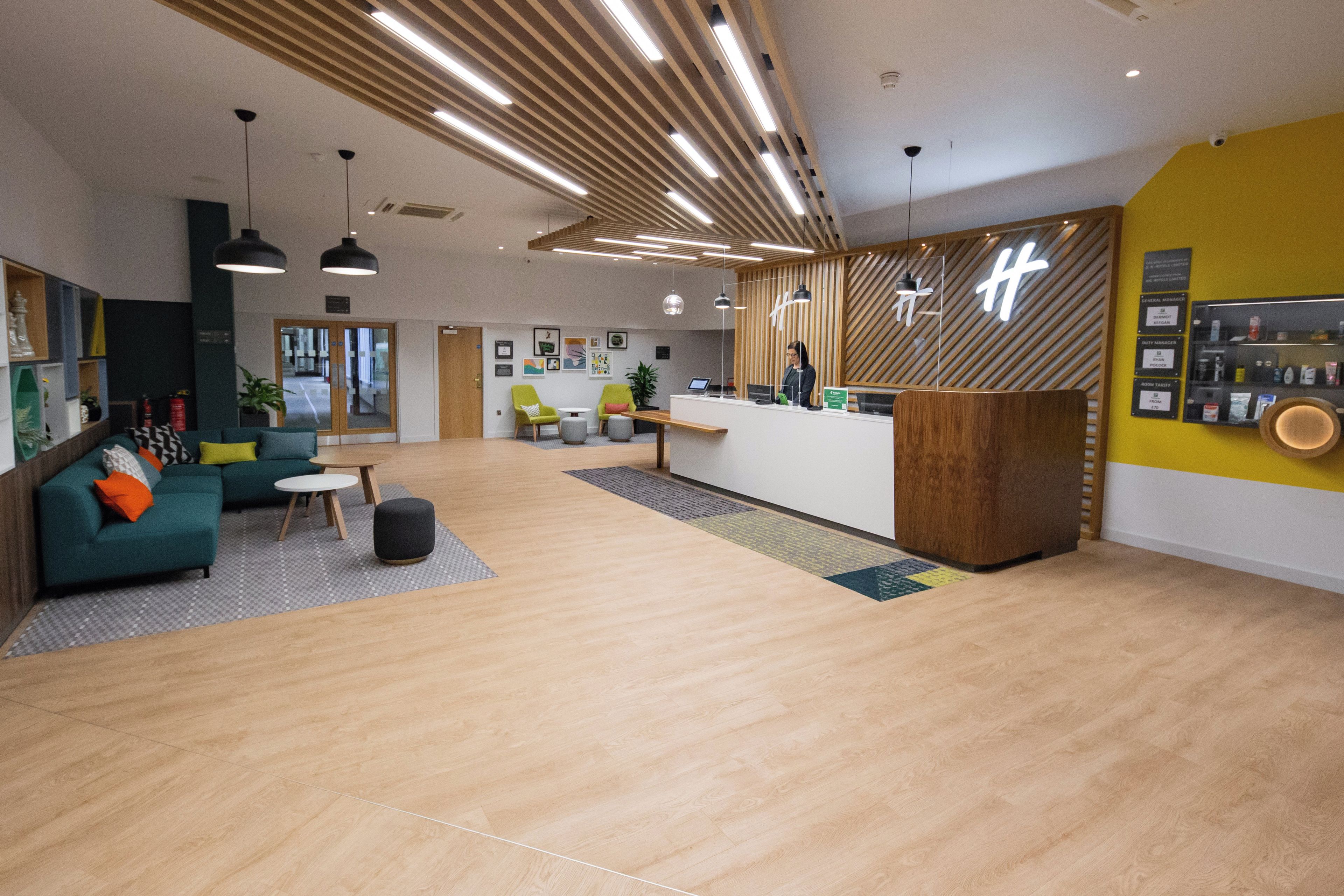 A modern hotel lobby with a reception desk, seating area, and a visible staircase.
