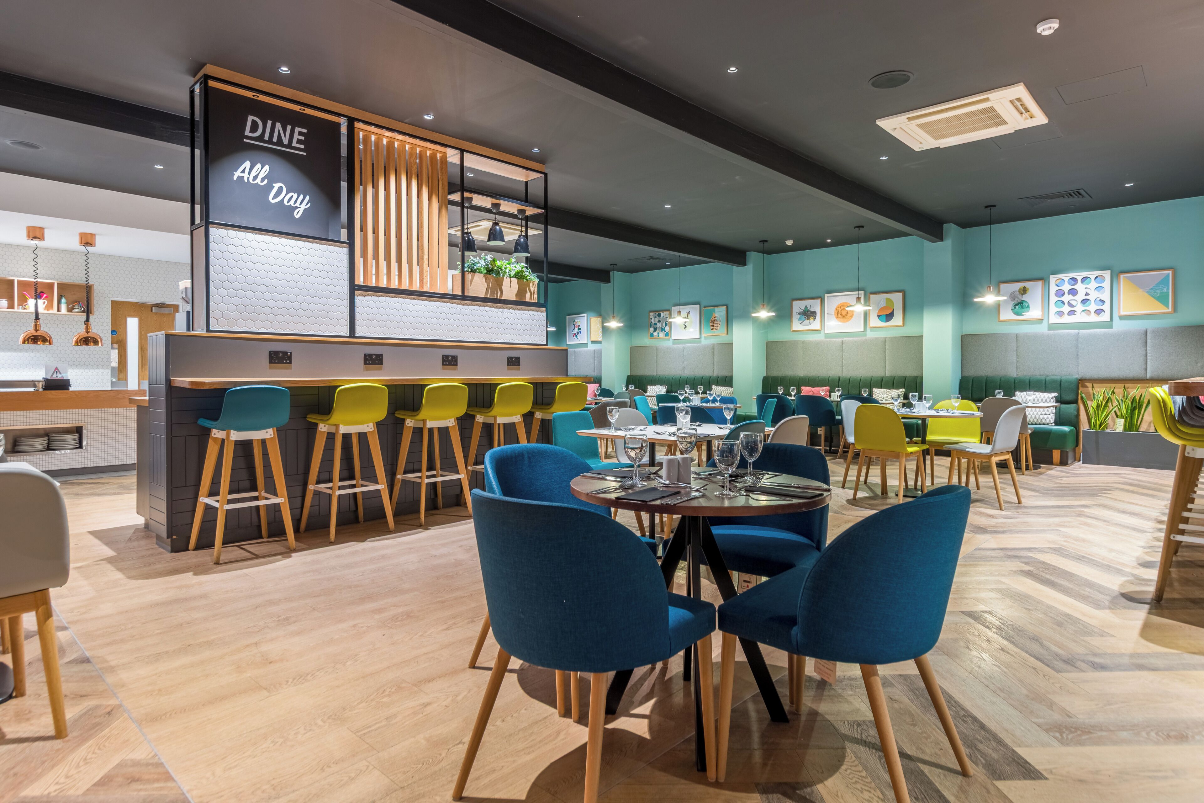 Un interior de restaurante moderno con área de bar, varias opciones de asientos como mesas redondas y taburetes, y diversa decoración en las paredes.