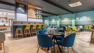 Un interior de restaurante moderno con área de bar, varias opciones de asientos como mesas redondas y taburetes, y diversa decoración en las paredes.