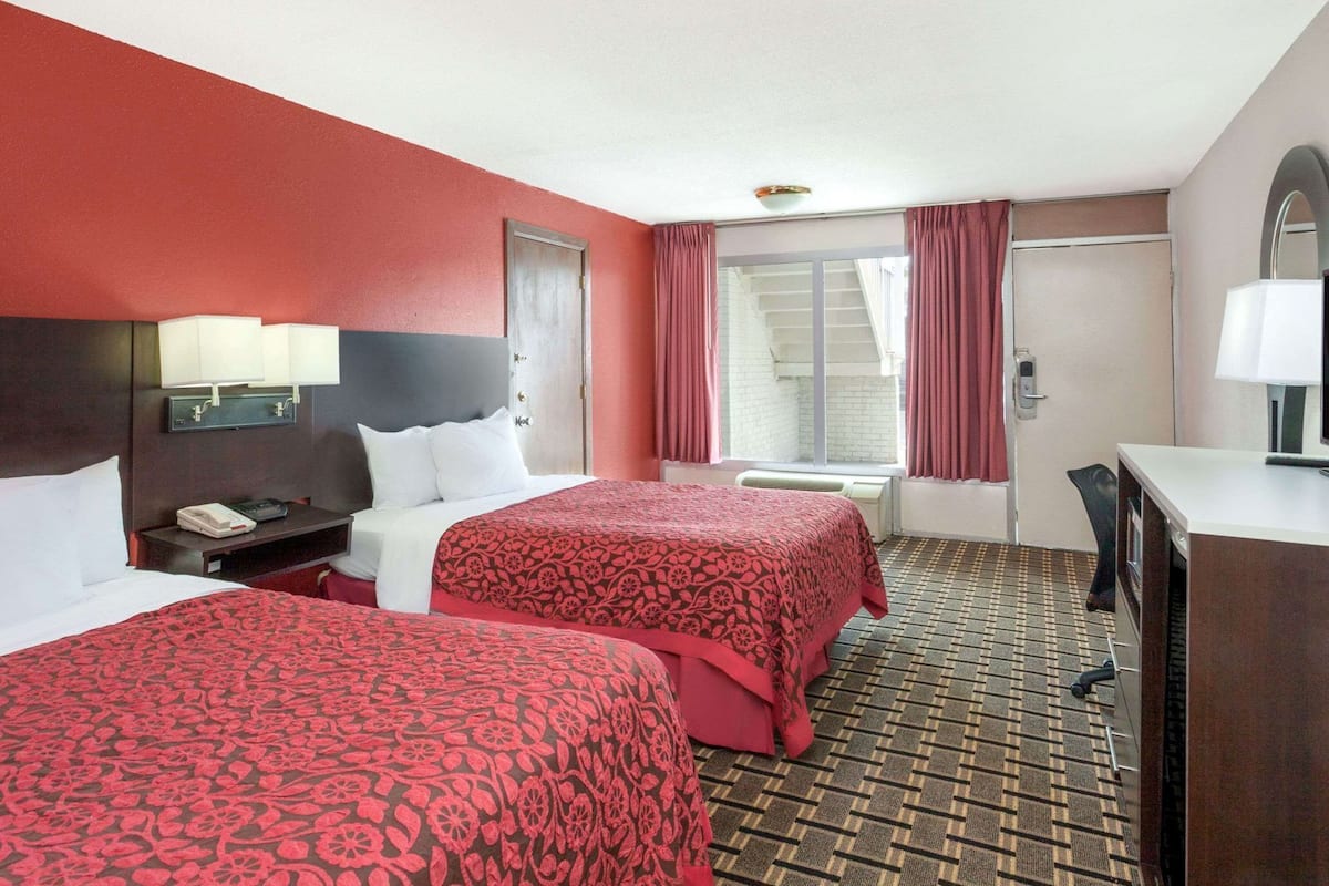 A hotel room with two beds, a desk, a chair, a telephone, and a window with curtains.