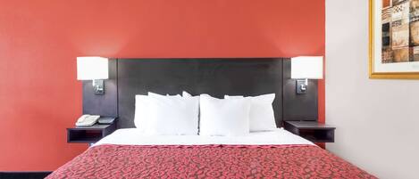 A hotel room with a red accent wall, a large bed with white bedding, two bedside tables with lamps, and a framed artwork on the wall.
