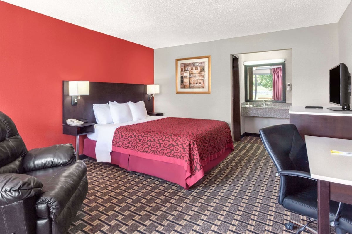 A hotel room with a bed, a desk, a chair, a couch, and a mirror.