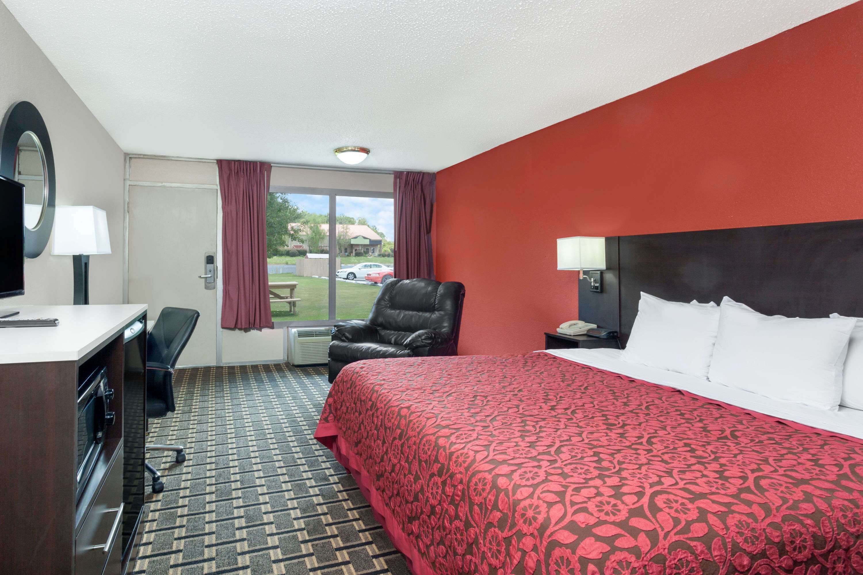 A hotel room with a bed, a desk, a chair, a TV, and a window with curtains.