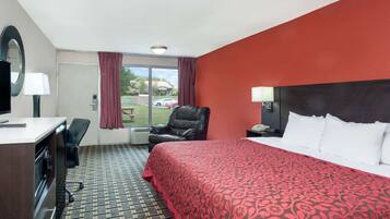 A hotel room with a bed, a desk, a chair, a TV, and a window with curtains.