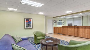 A lobby with a blue patterned carpet, a green sofa, a green armchair, and a wooden reception desk. - Days Inn by Wyndham Cullman (Cullman)