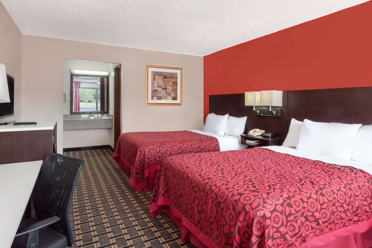 A hotel room with two beds, a desk, a chair, a mirror, and a window.