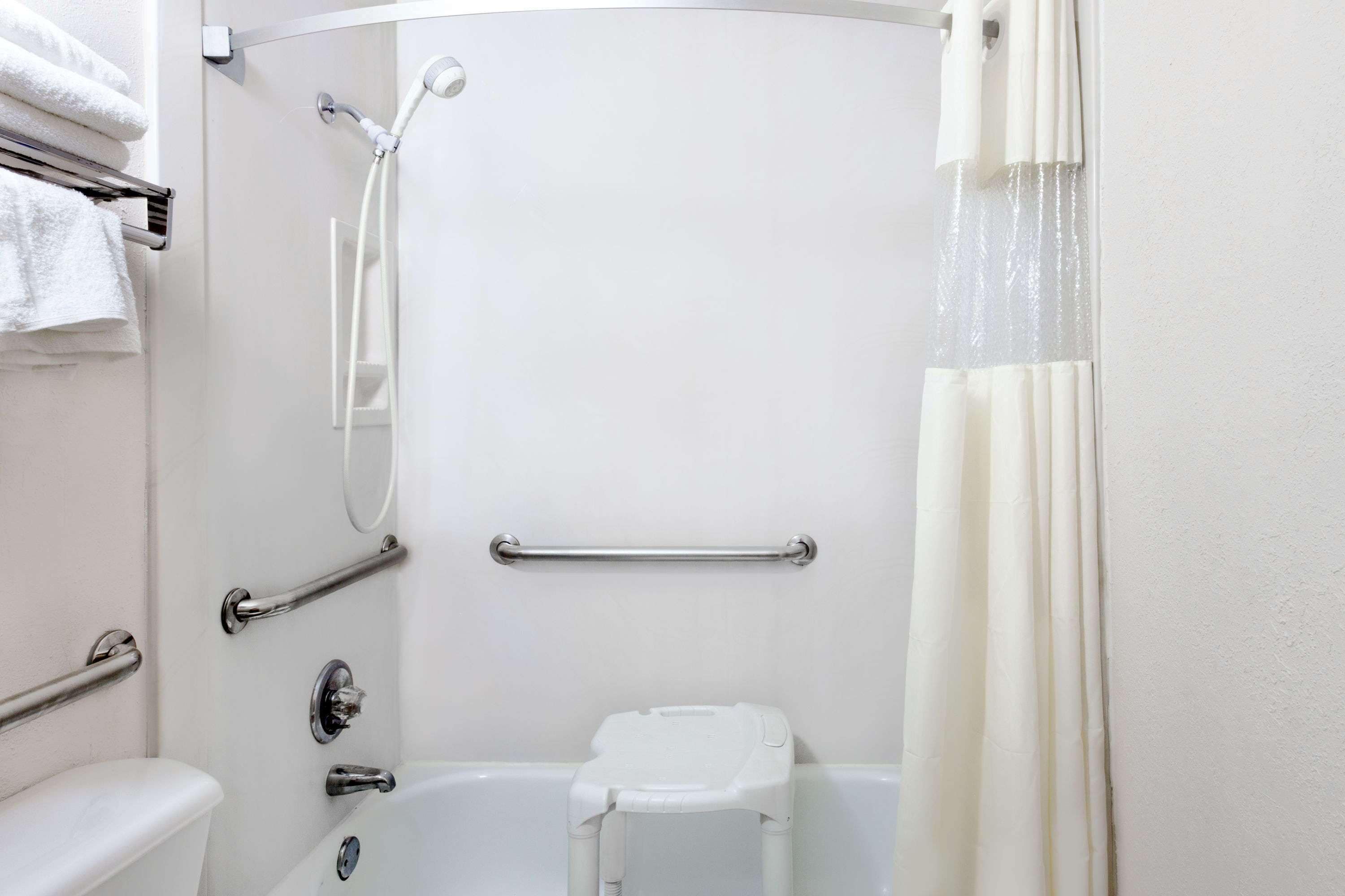 A bathroom with a shower, toilet, and grab bars.