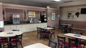 A cafeteria with multiple tables and chairs, a counter with beverages, and a sign indicating breakfast service. - Days Inn by Wyndham Cullman (Cullman)