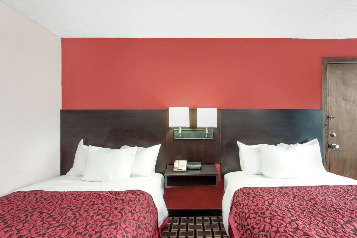 A hotel room with two beds, a red and black color scheme, a small table with a phone and a lamp, and a wooden door.
