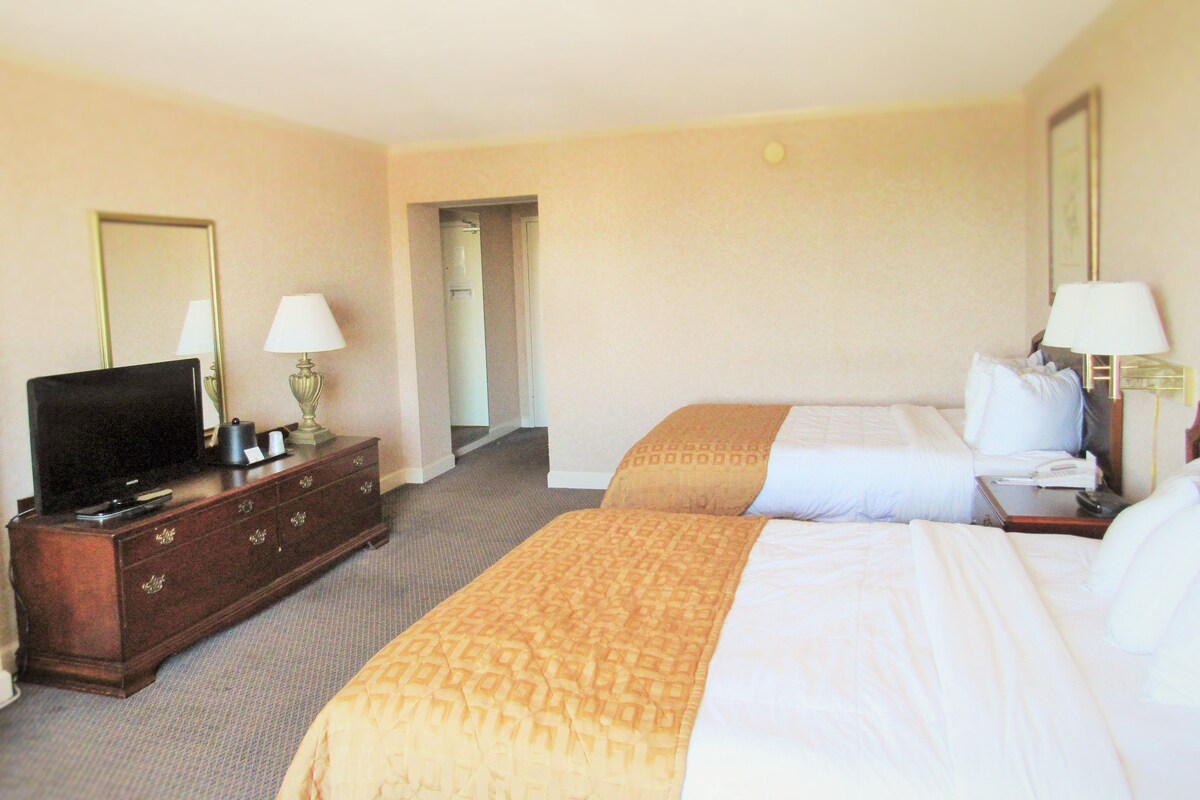 A hotel room with a bed, a TV on a dresser, and a lamp.