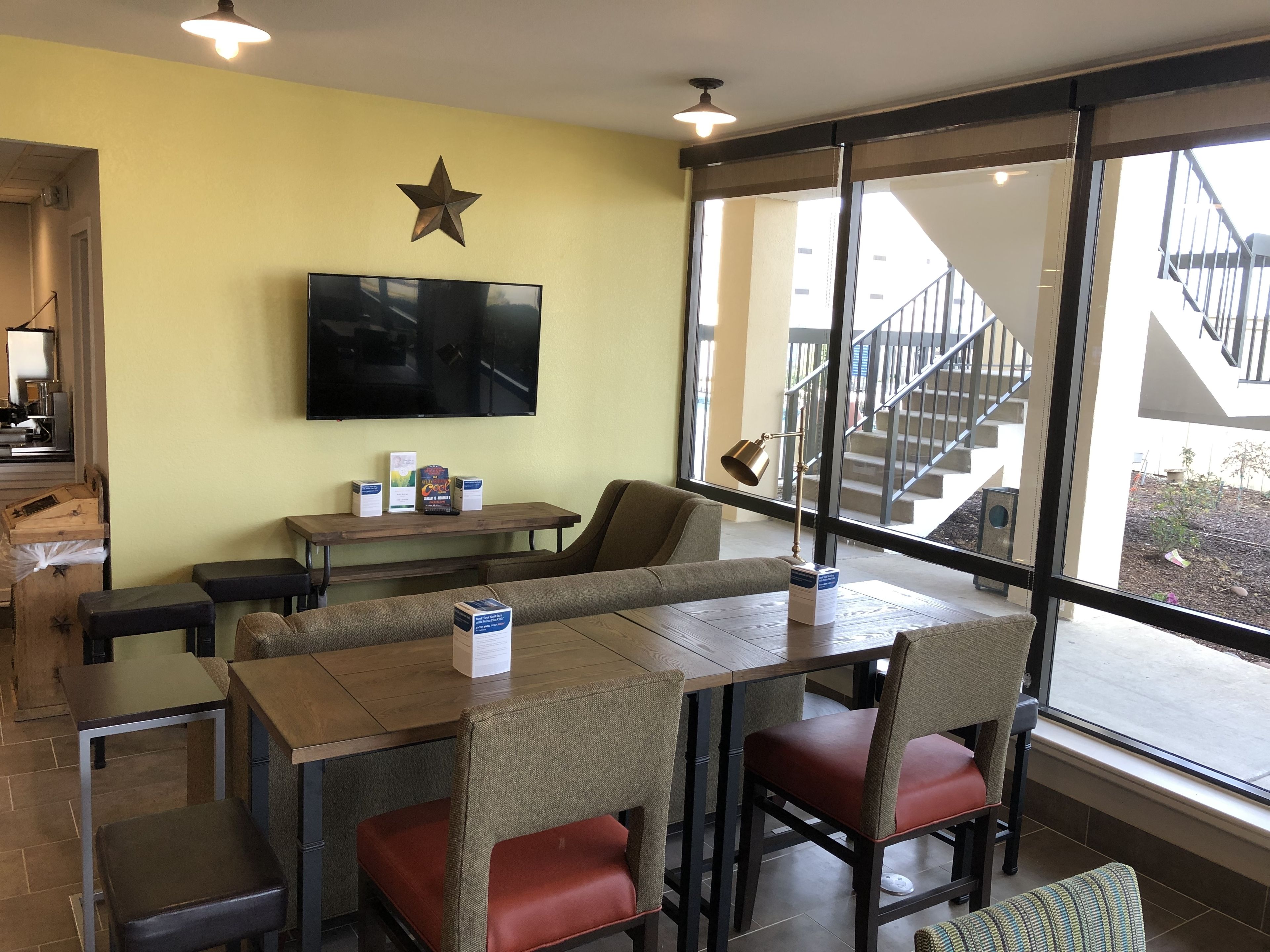 A restaurant with a large window, a star decoration on the wall, and a television mounted above a wooden table.