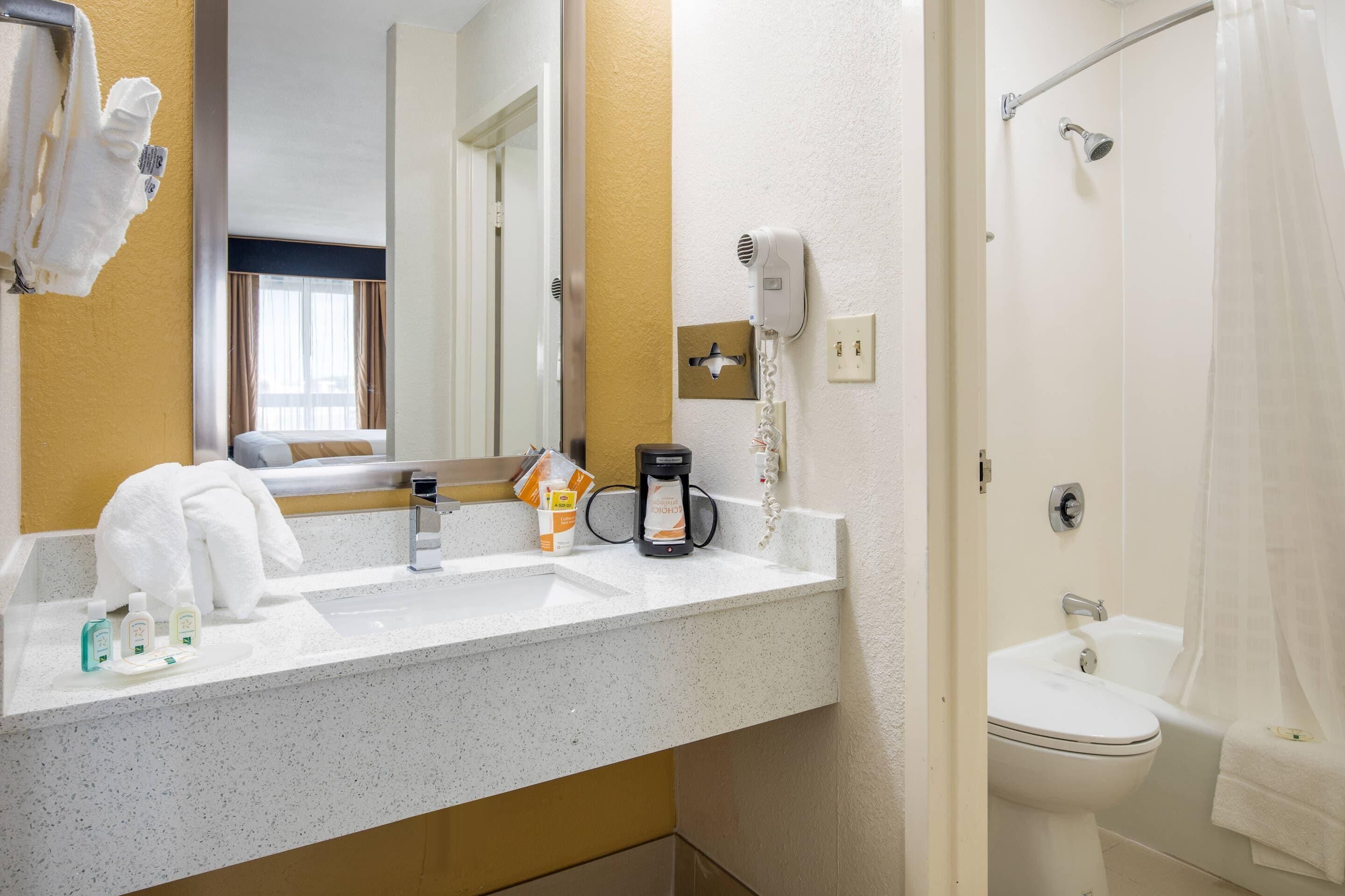 Un baño de hotel con lavamanos, espejo, toallero, ducha y cafetera.