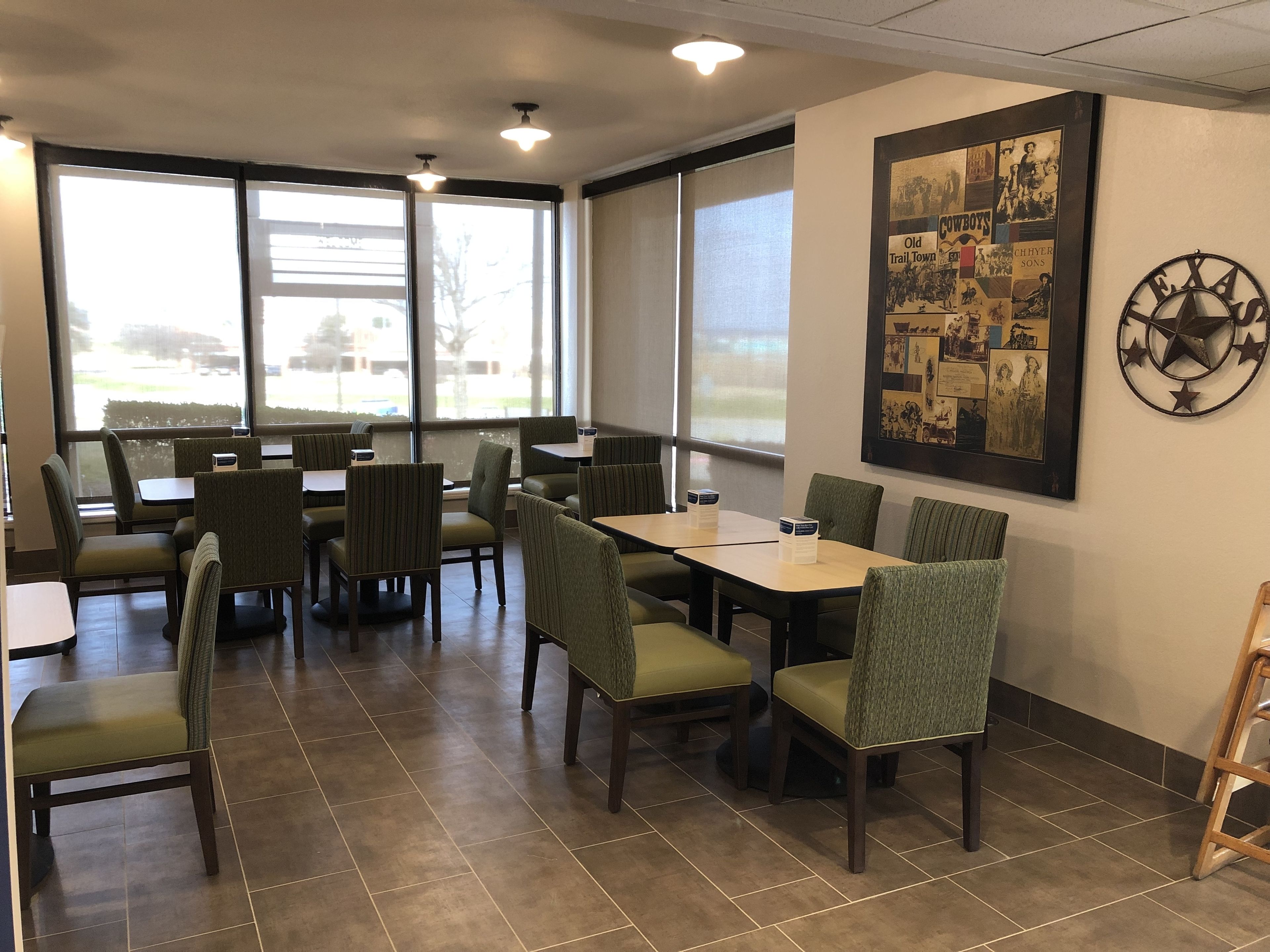 Un restaurante con cabinas y mesas, ventanas amplias y una pared decorada con un collage enmarcado.