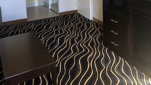 A hotel room with a kitchenette, a dining area with a patterned rug, a TV, and a framed picture on the wall.