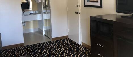 Ein Hotelzimmer mit Küchenzeile, einem Essbereich mit gemustertem Teppich, einem Fernseher und einem gerahmten Bild an der Wand.
