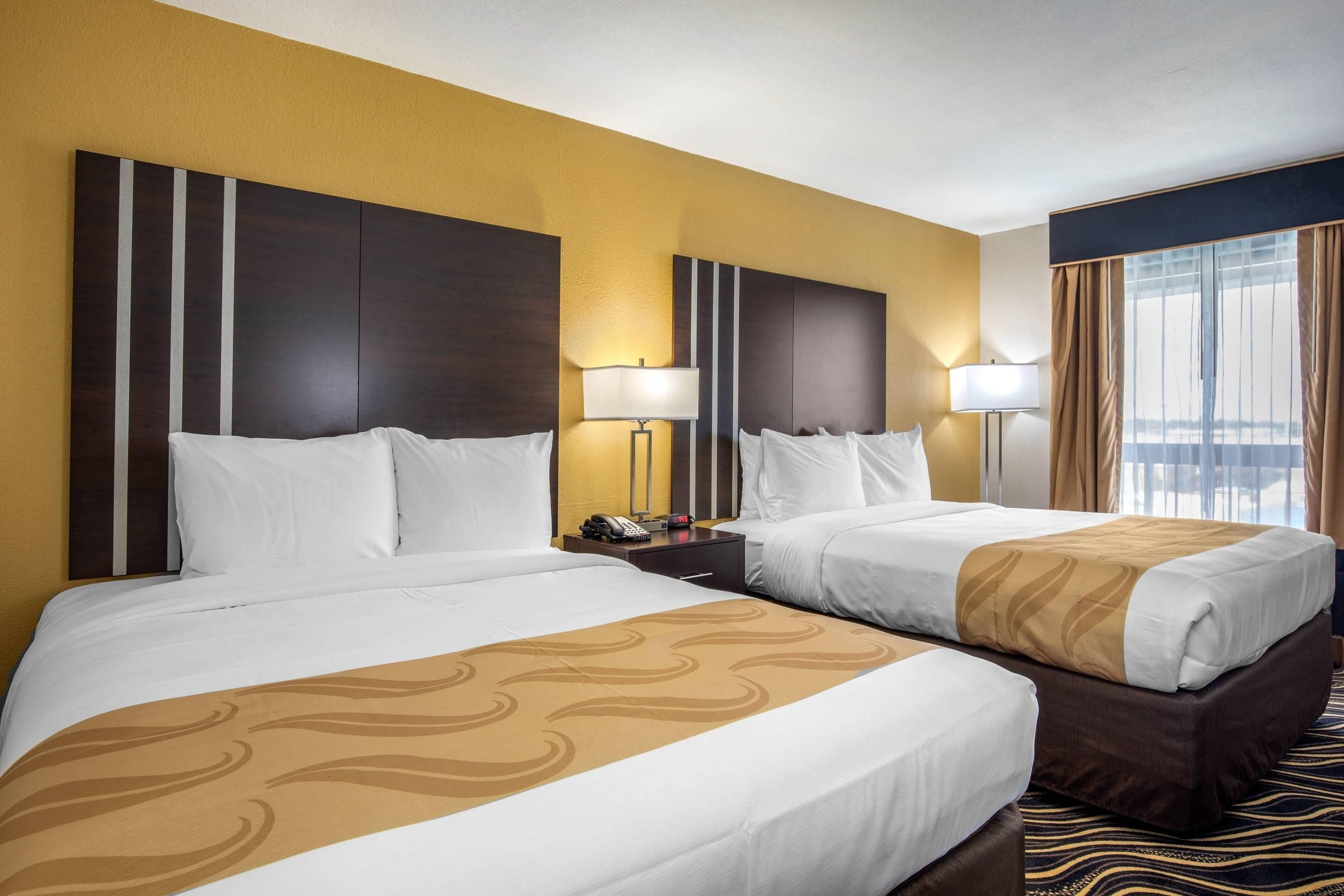 Quarto de hotel com duas camas, uma mesa de cabeceira com telefone e uma janela com cortinas.