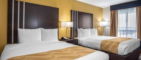 Quarto de hotel com duas camas, uma mesa de cabeceira com telefone e uma janela com cortinas.