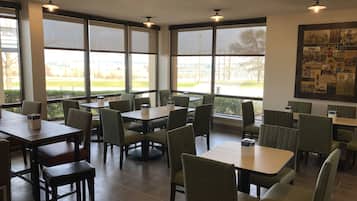 A restaurant with large windows, green upholstered chairs, and tables with menus.
