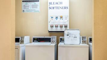 A laundry facility with multiple washing machines and a sign above them advertising soap, bleach, and softeners.