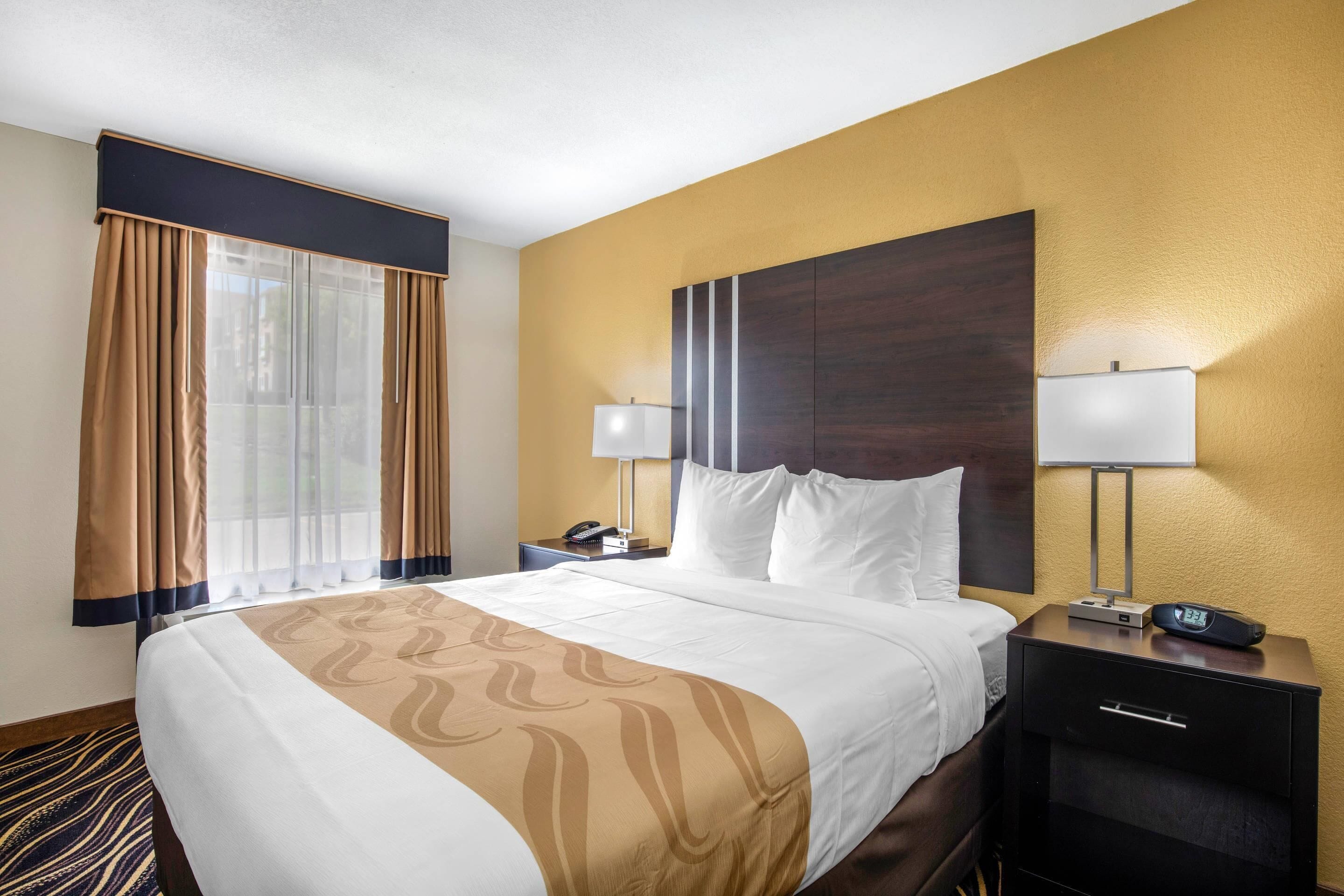 A hotel room with a large bed, two bedside tables, a nightstand, a lamp, and a clock.
