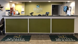 A reception desk at Quality Inn & Suites with a check-in counter, a digital kiosk, and a reception area with a green wall and ceiling lights.