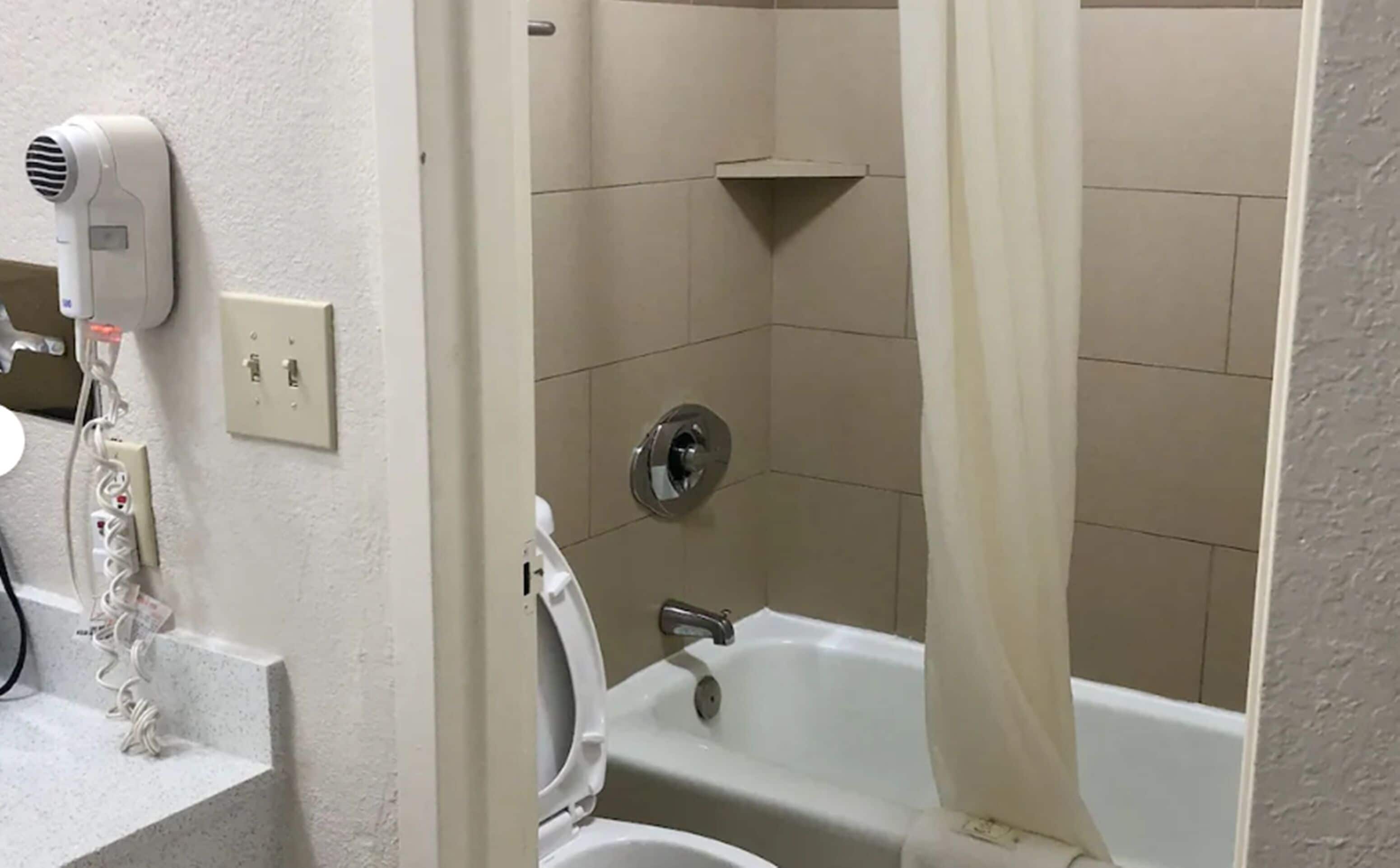 Un baño con bañera, ducha y secador de pelo en la pared.