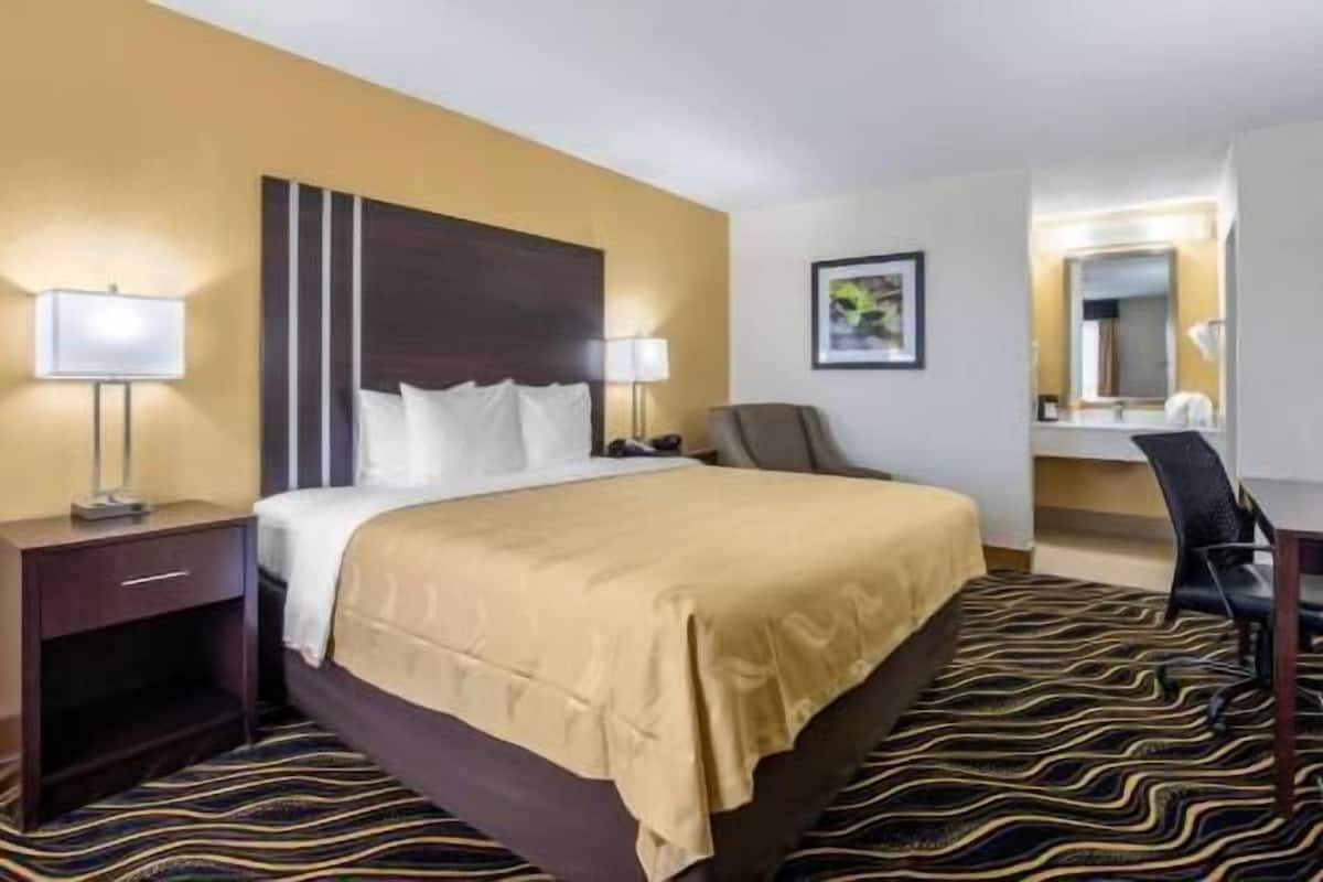 A hotel room with a bed, bedside lamps, a chair, a desk, and a mirror.
