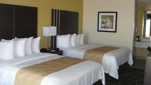 A hotel room with two beds, a nightstand, a lamp, a framed picture on the wall, and a bathroom mirror.