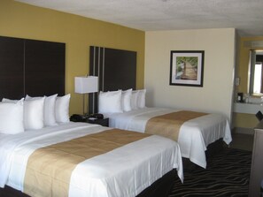 A hotel room with two beds, a nightstand, a lamp, a framed picture on the wall, and a bathroom mirror. - Quality Inn West Fort Worth (Fort Worth)