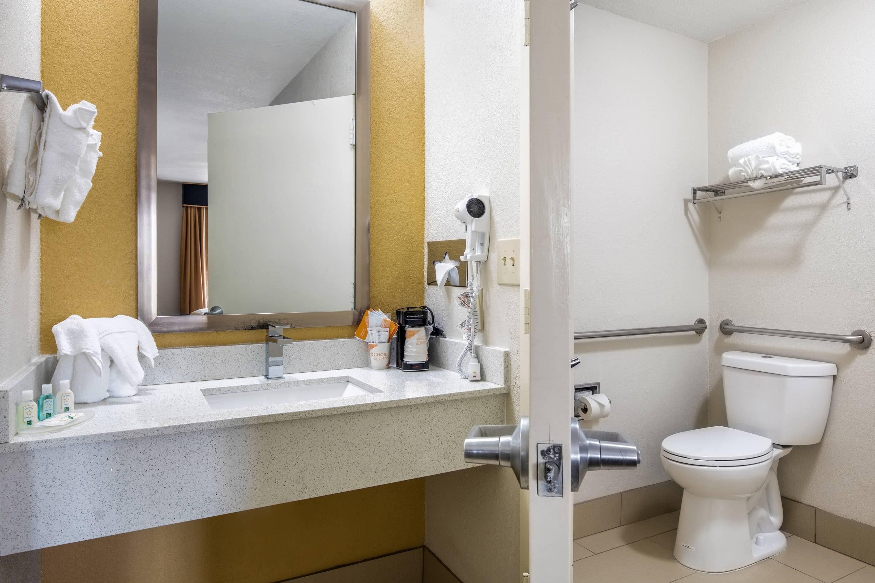A bathroom with a white sink, mirror, and toilet. There are towels and toiletries on the counter.