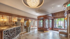 Um hall espaçoso com piso de mármore, um lustre imponente e uma recepção com detalhes em madeira ornamental.