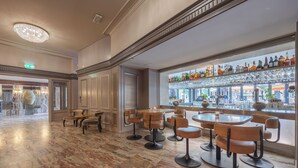 Uma área de bar com piso de mármore, cadeiras de madeira e uma vitrine de garrafas.
