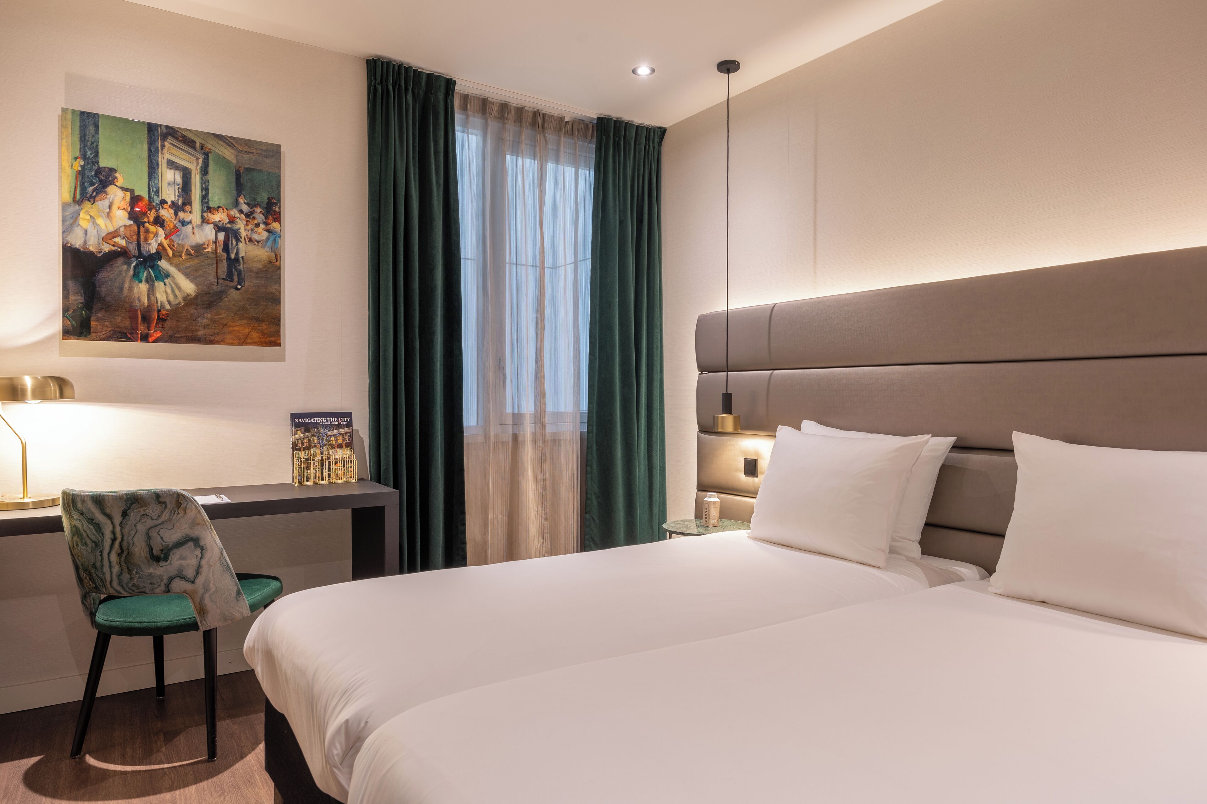 Une chambre d’hôtel avec un grand lit, un bureau avec une chaise, un tableau au mur et une fenêtre avec des rideaux.