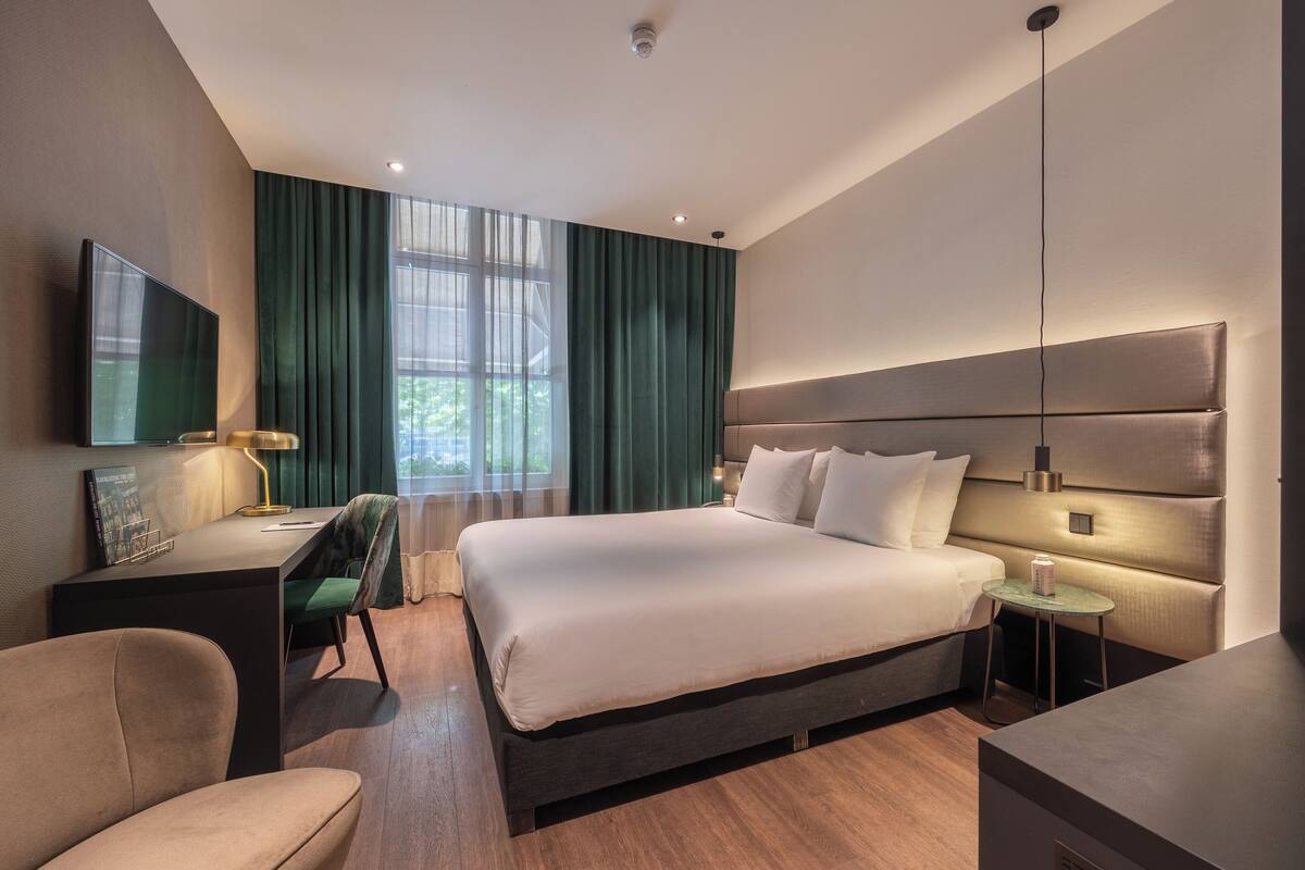 A modern hotel room with a large bed, a desk, a chair, and a TV.
