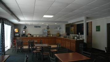 A restaurant with a kitchen area, wooden tables and chairs, and a 'Welcome' sign on the wall.