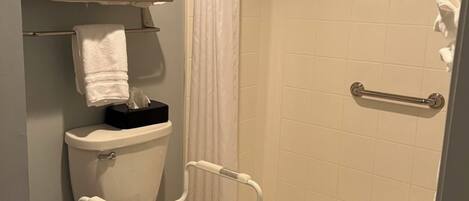 A bathroom with a toilet, a shower with a grab bar, and a towel rack with folded towels.