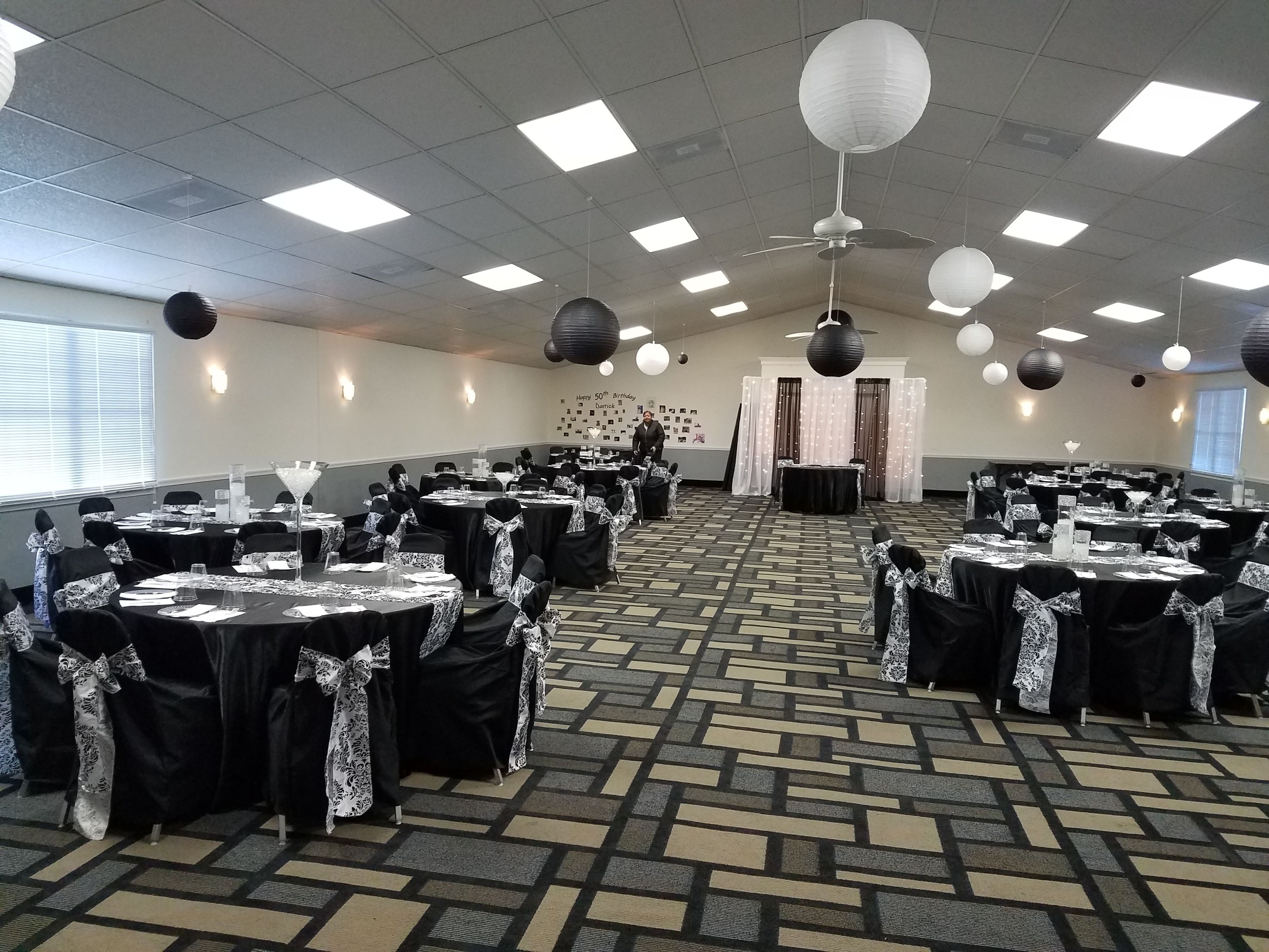 A banquet hall with tables set for a formal event, featuring a patterned carpet and ceiling lights.