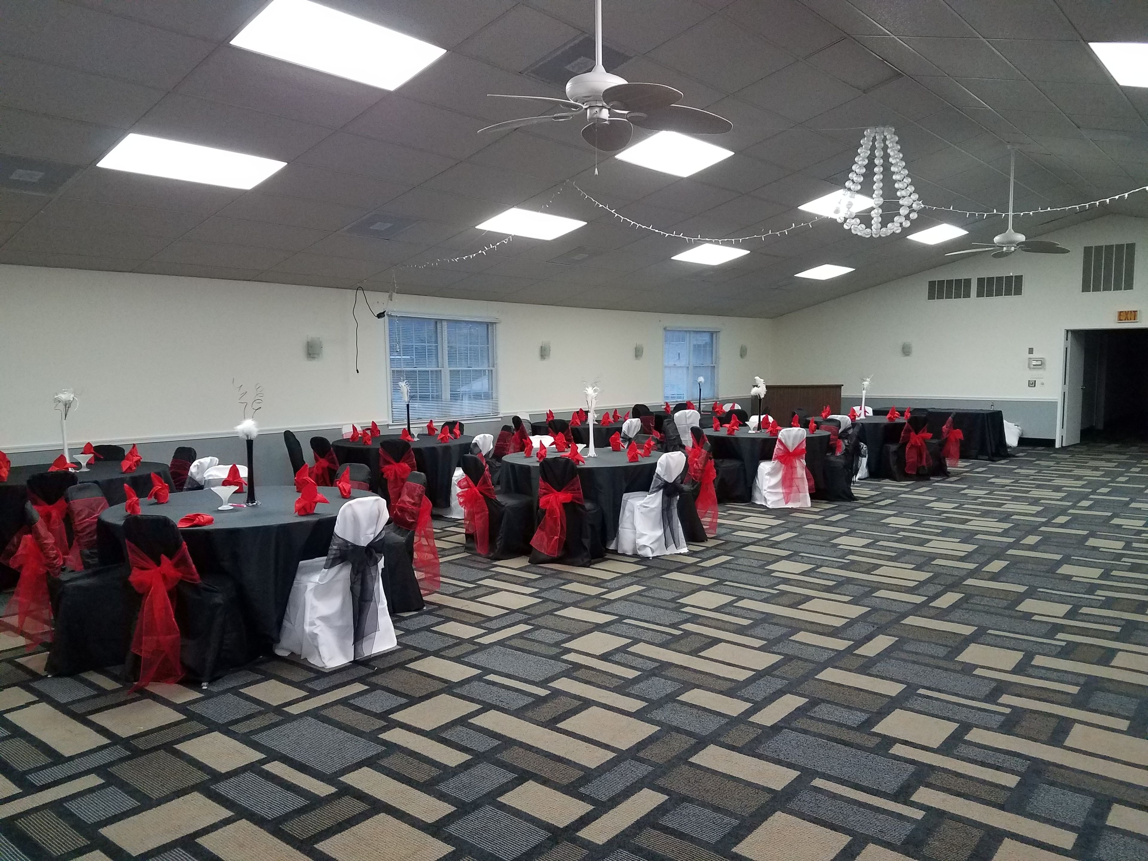 Un salón de conferencias con mesas dispuestas en filas, cada una cubierta con un mantel negro y cintas rojas.
