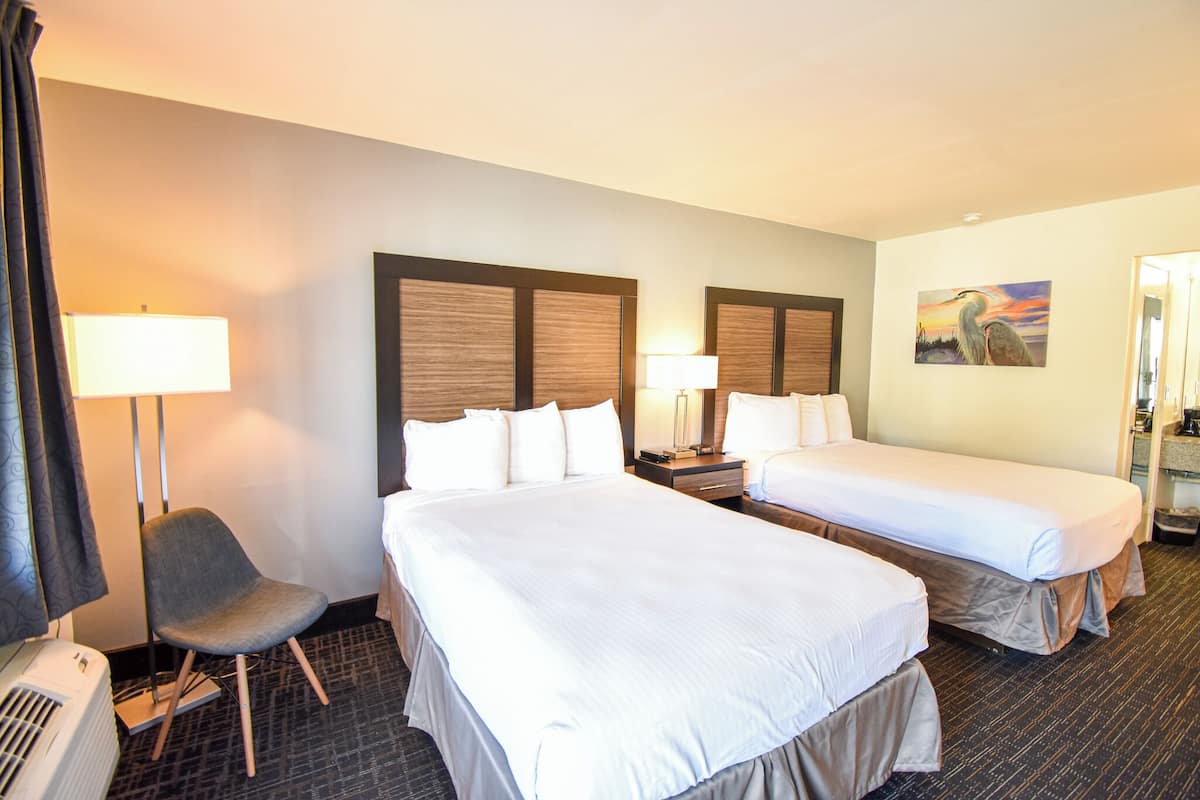 A hotel room with two beds, a chair, and a painting on the wall.