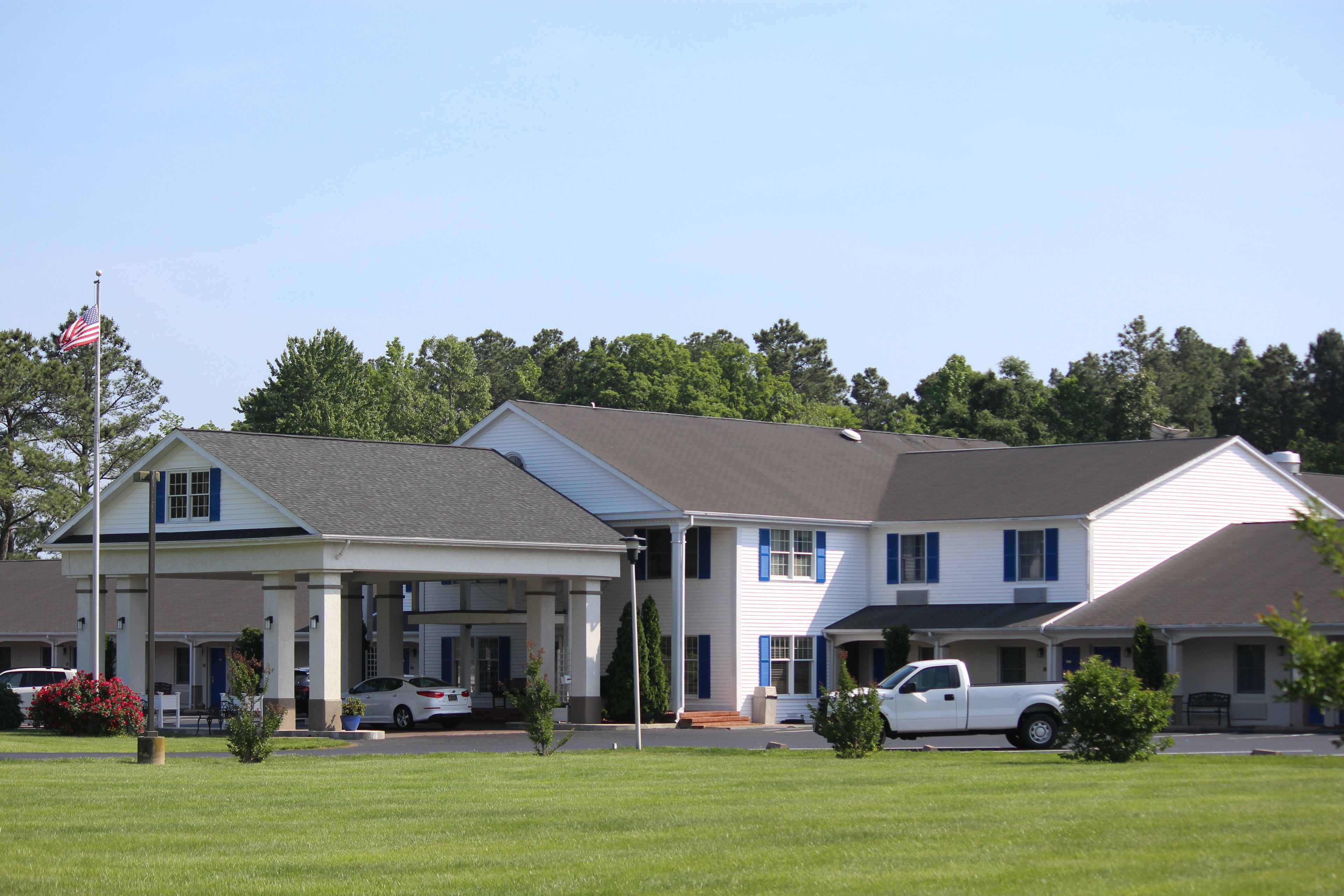 A motel with a covered front porch, a flagpole with an American flag, and a white pickup truck parked in front.